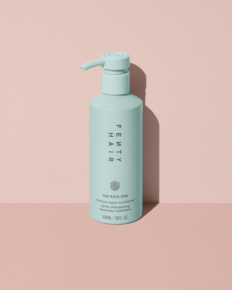 Fenty Hair The Rich One Moisture Repair Conditioner aluminum bottle with a pump on a pink background.