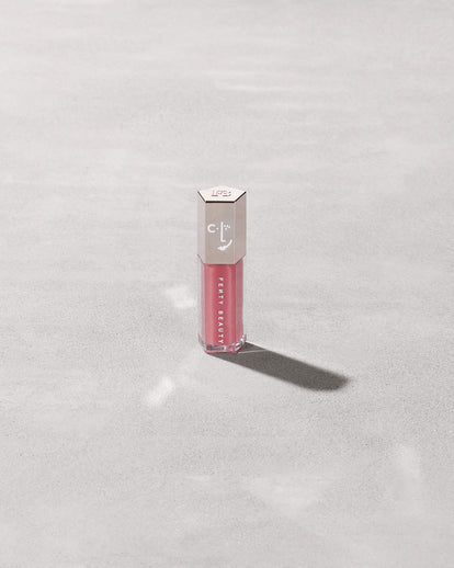 A closed tube of Gloss Bomb Universal Lip Luminizer in the shade Candy Soda on a grey background.